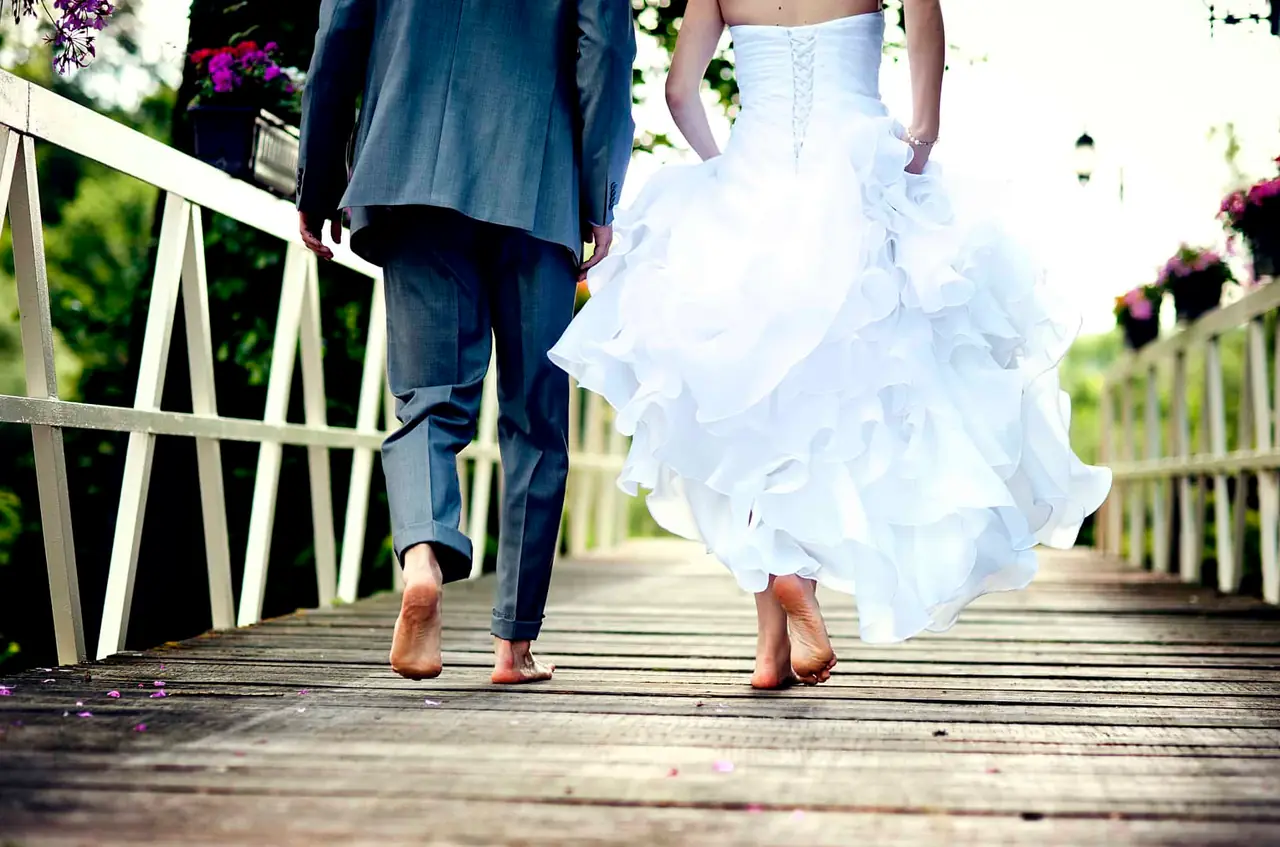 A barefoot wedding couple walk together along a timber bridge.
