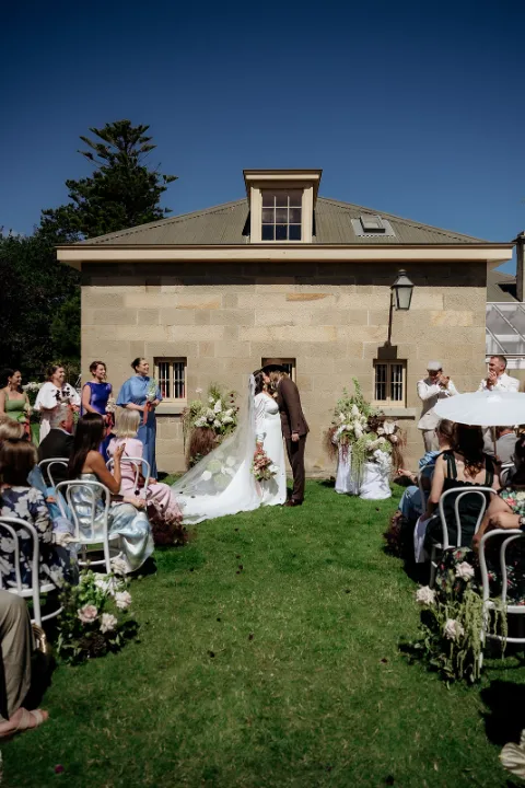 First kiss at outdoor garden style wedding in front of sandstone building in Hobart, tasmania